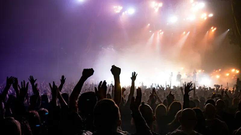 Público con las manos en alto ante un escenario con focos en un concierto