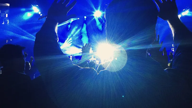 Silueta de un espectador con las manos en alto ante los focos azules de un gran concierto