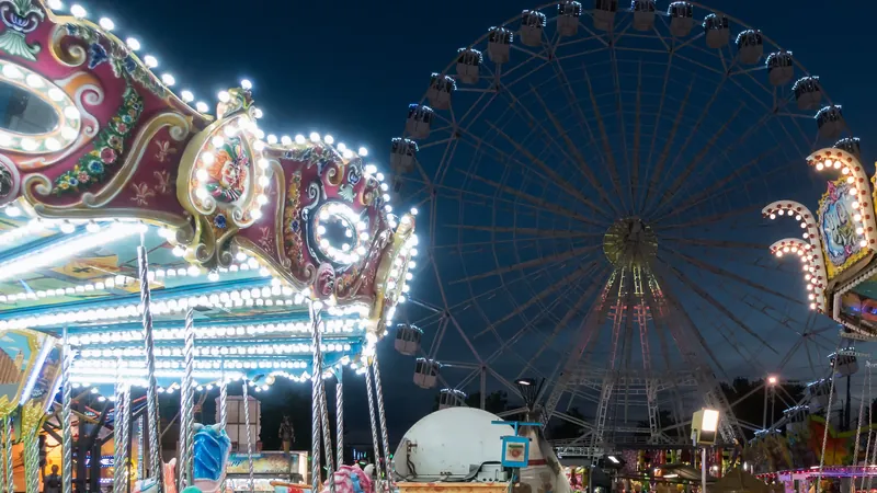 Recinto ferial de noche con tiovivo iluminado, noria al fondo y gente paseando entre las atracciones