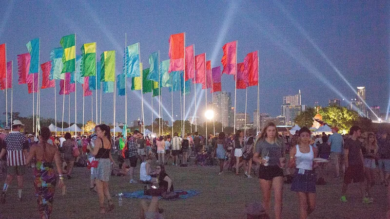 Banderas de colores y haces de luz sobre el público de un festival de música al anochecer