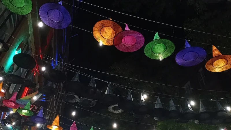Sombreros de bruja de colores iluminados colgando sobre una calle de noche en Halloween