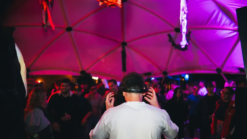 DJ de espaldas pinchando ante el público bajo una carpa iluminada de rosa