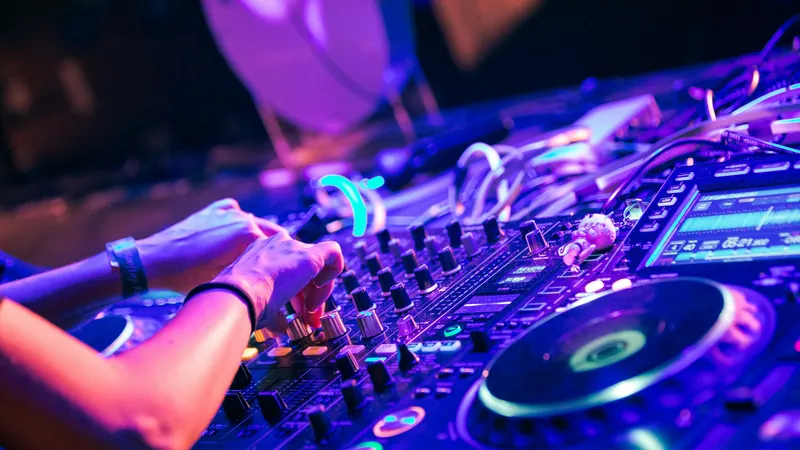 Manos de un DJ sobre la mesa de mezclas bajo luces violetas