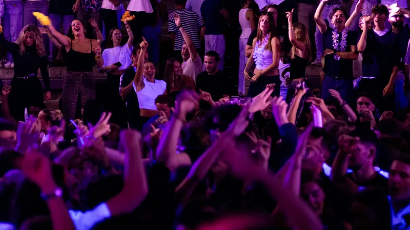 Pista de baile llena de gente bailando bajo luces de discoteca violetas