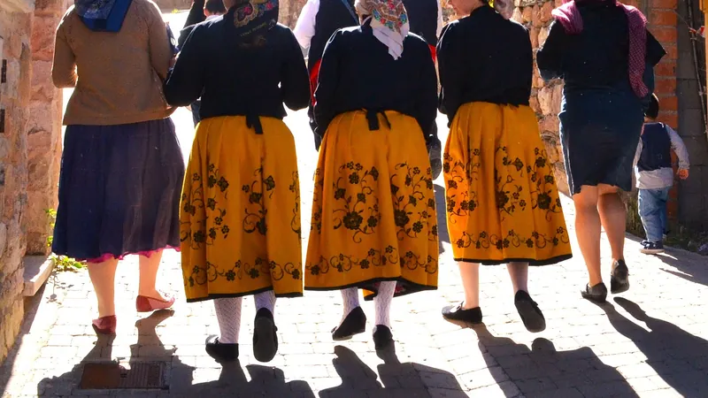 Mujeres con faldas tradicionales bordadas caminando de espaldas por una calle empedrada de Atienza a contraluz