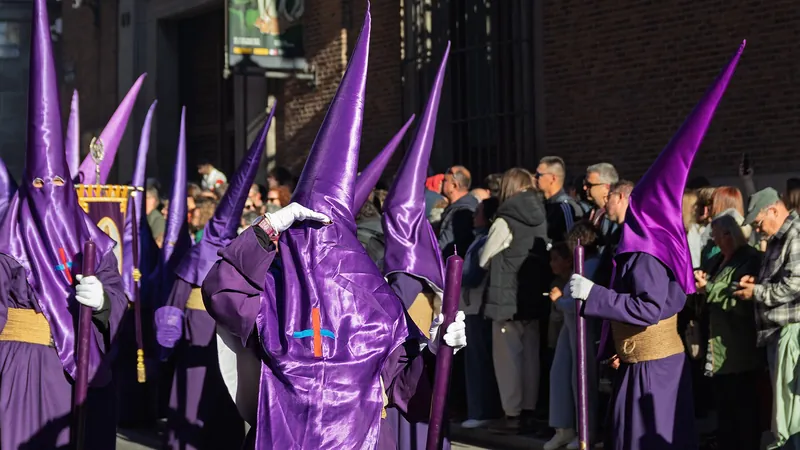 Nazarenos con capirote morado en una procesión de Semana Santa por una calle de Madrid
