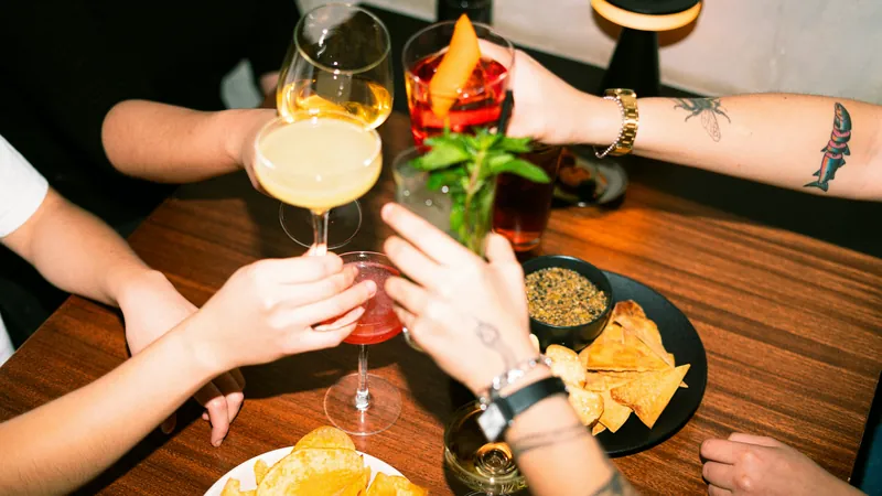 Brindis de amigos con cócteles y aperitivos sobre una mesa de madera